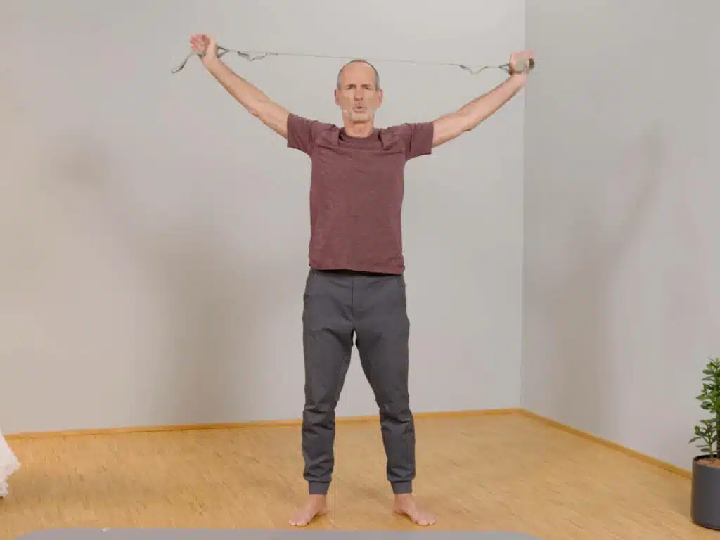 Roland Liebscher-Bracht hat die Arme über den Kopf nach hinten gestreckt und hält mit beiden Händen einen hellgrünen Trainingsgurt auf Spannung.