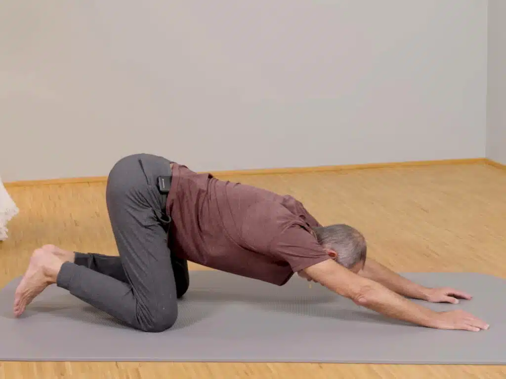 Roland Liebscher-Bracht kniet am Boden und stützt sich mit ausgestreckten Armen am Boden ab, um seine Brust zu dehnen.