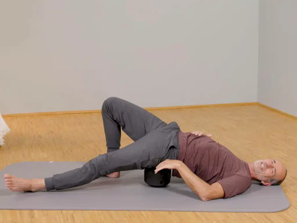 Roland Liebscher-Bracht liegt am Boden auf einer Übungsmatte und hat sein Gesäß auf dem ISG-Ischias-Retter platziert.