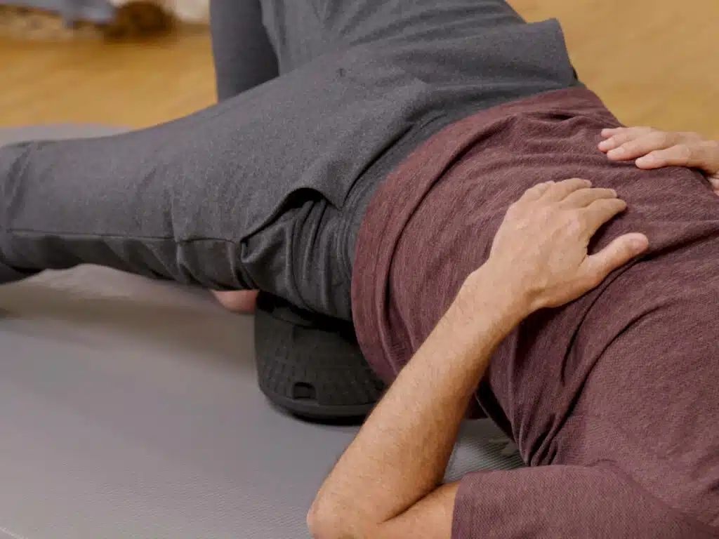 Eine Person liegt mit dem Gesäß während einer Übung auf dem ISG-Ischias-Retter von Liebscher & Bracht.