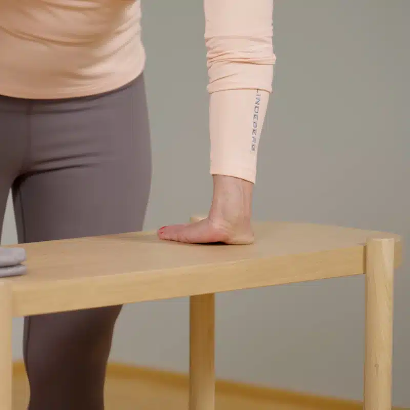 Eine Person hat ihre Hand auf einen Tisch abgelegt. Die Finger schauen zu ihren Beinen zurück, das Handgelenk ist vorne.