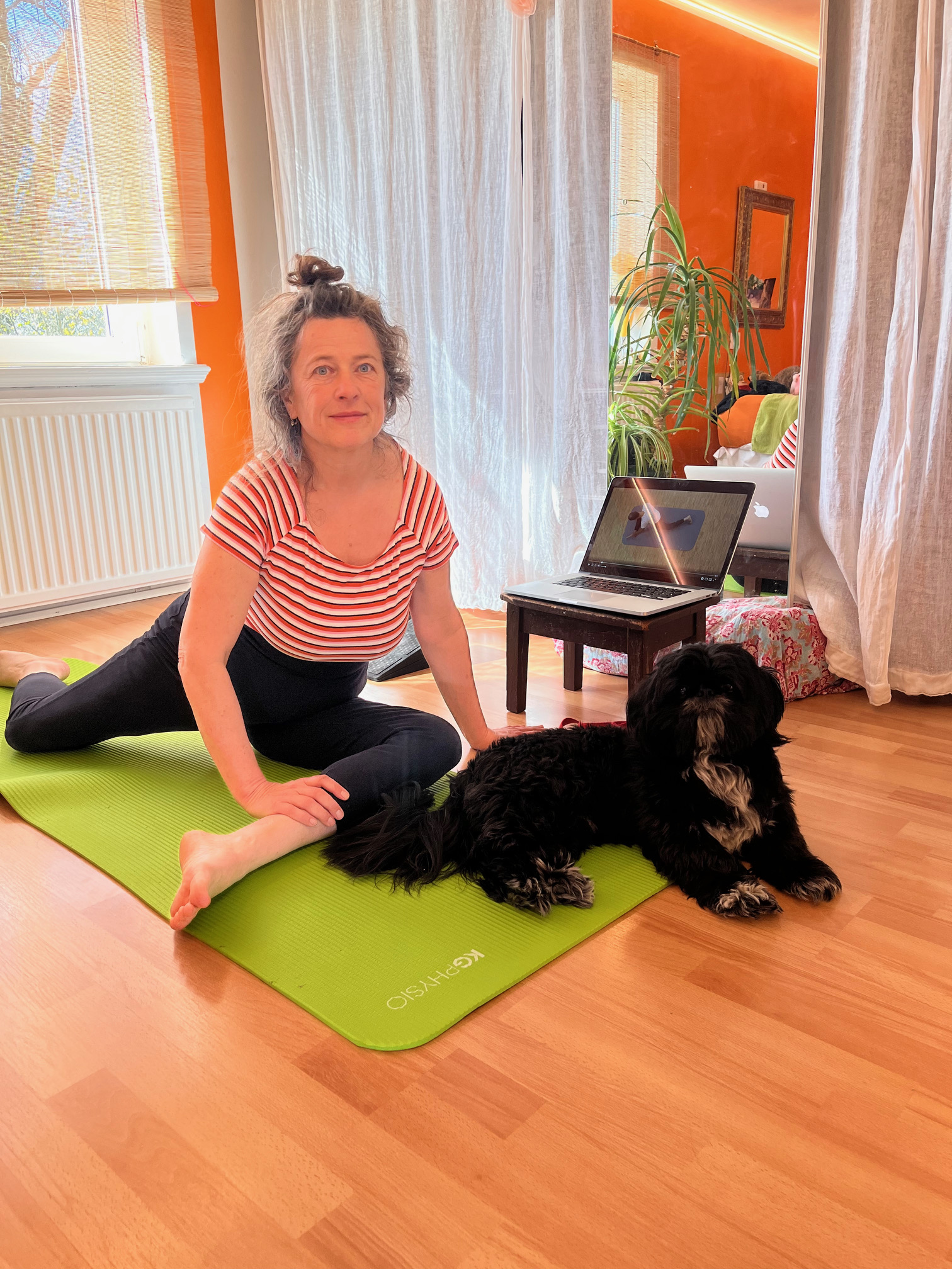 Yvonne sitzt auf der Übungsmatte. Ein schwarzer Hund liegt daneben