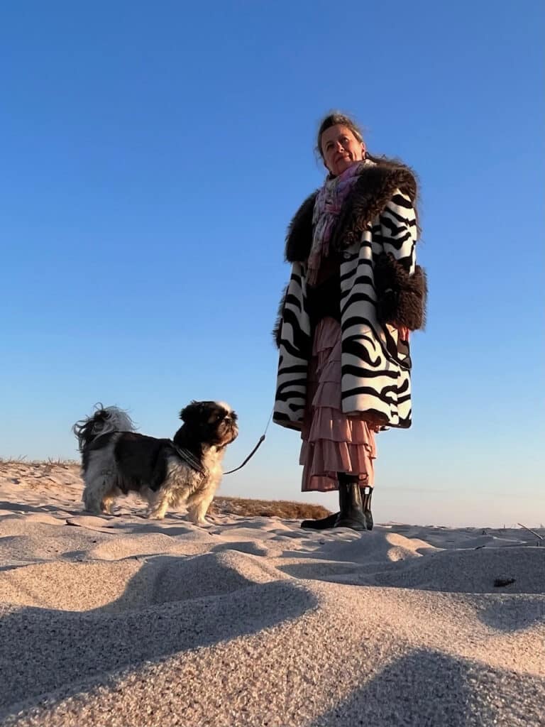 Yvonne steht mit ihrem Hund vor einem blauen Himmel