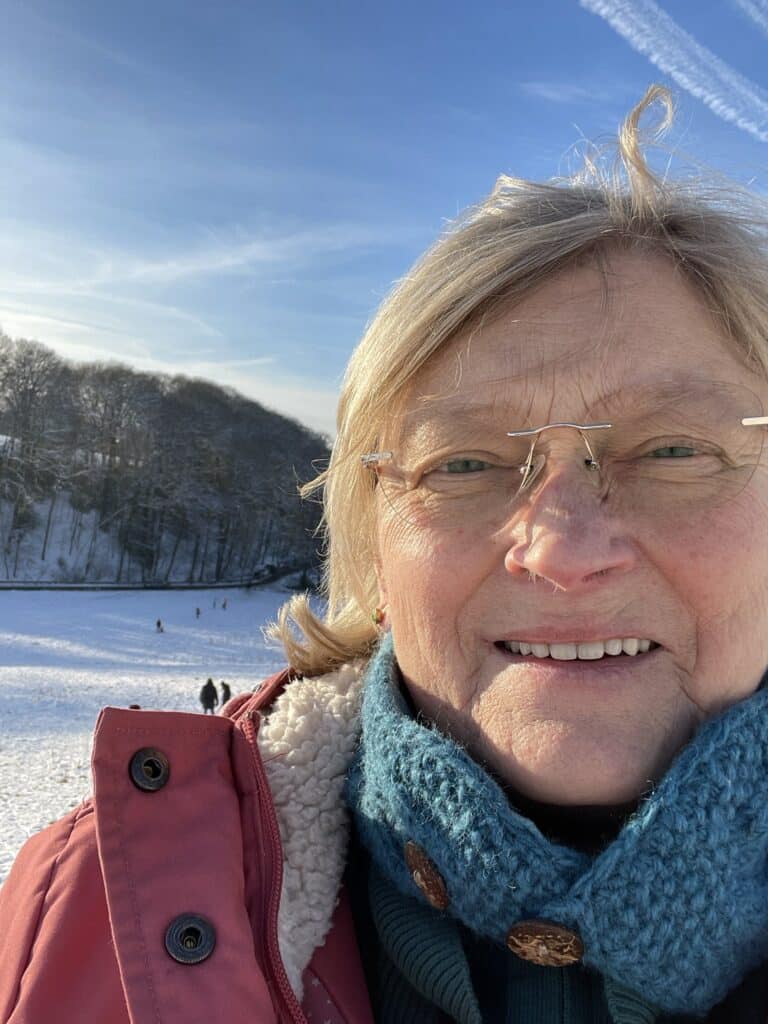 Gudrun steht vor einer verschneiten Landschaft und sieht in die Kamera