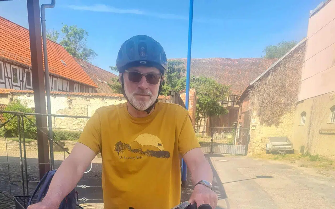 Rainer steht vor einem Bauernhof und sieht in die Kamera