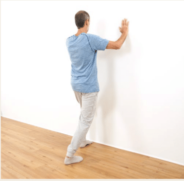 Bei Schmerzen in der Ferse kannst du die Wade dehnen, indem du dich an die Wand stellst.